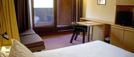 A hotel room with a bed, a desk, a chair, a television, and a window with curtains.
