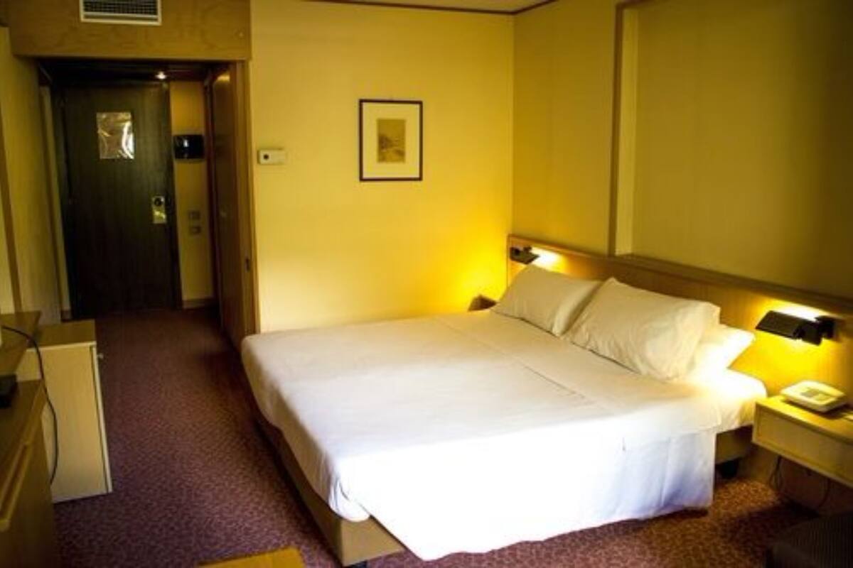 Une chambre d’hôtel avec un lit, une lampe de chevet et un petit bureau avec un téléphone.