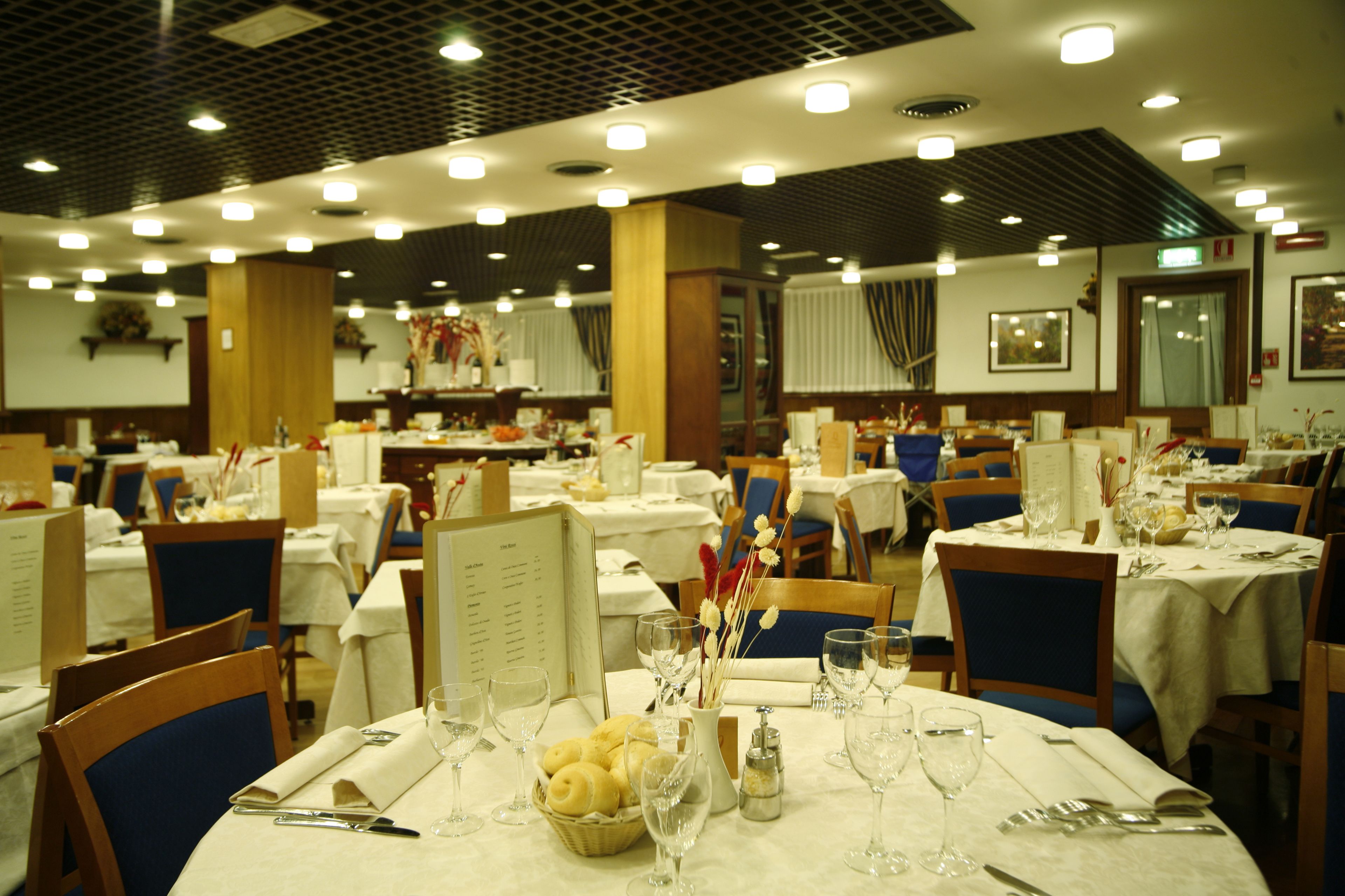 Un restaurante con varias mesas preparadas para comer, cada una con un atril para el menú, copas de vino y una cesta de pan.