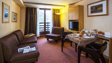 Une chambre d’hôtel avec un canapé, une petite table avec une lampe, une table à manger dressée avec des assiettes et des tasses, et un téléviseur posé sur un meuble.