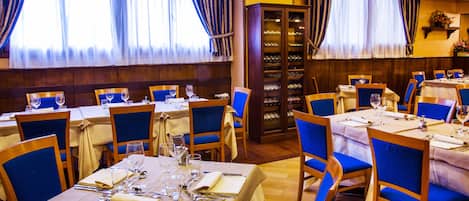 A restaurant with multiple tables set for dining, blue chairs, and a wine cabinet.