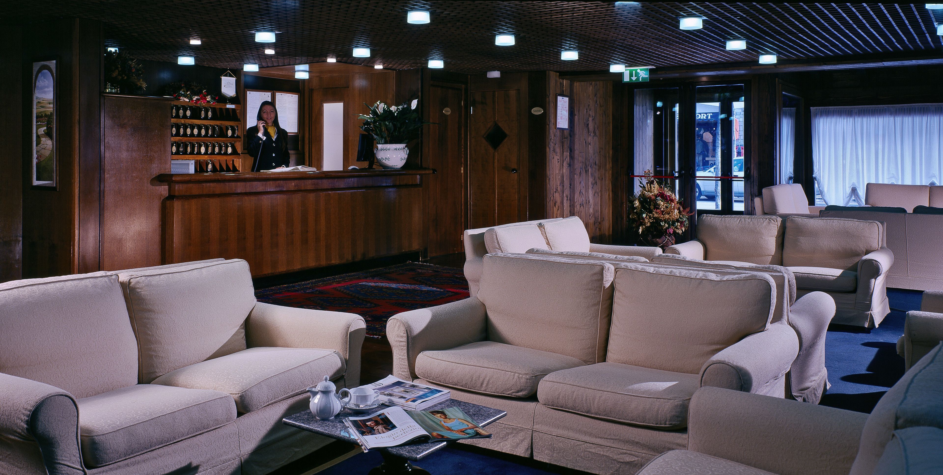 A hotel lobby with a reception desk, seating area, and a view of the street through the glass door.