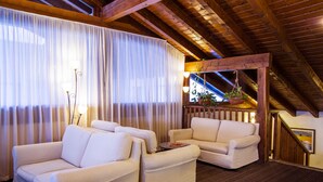 A cozy room with two white sofas, a wooden ceiling, and a staircase.