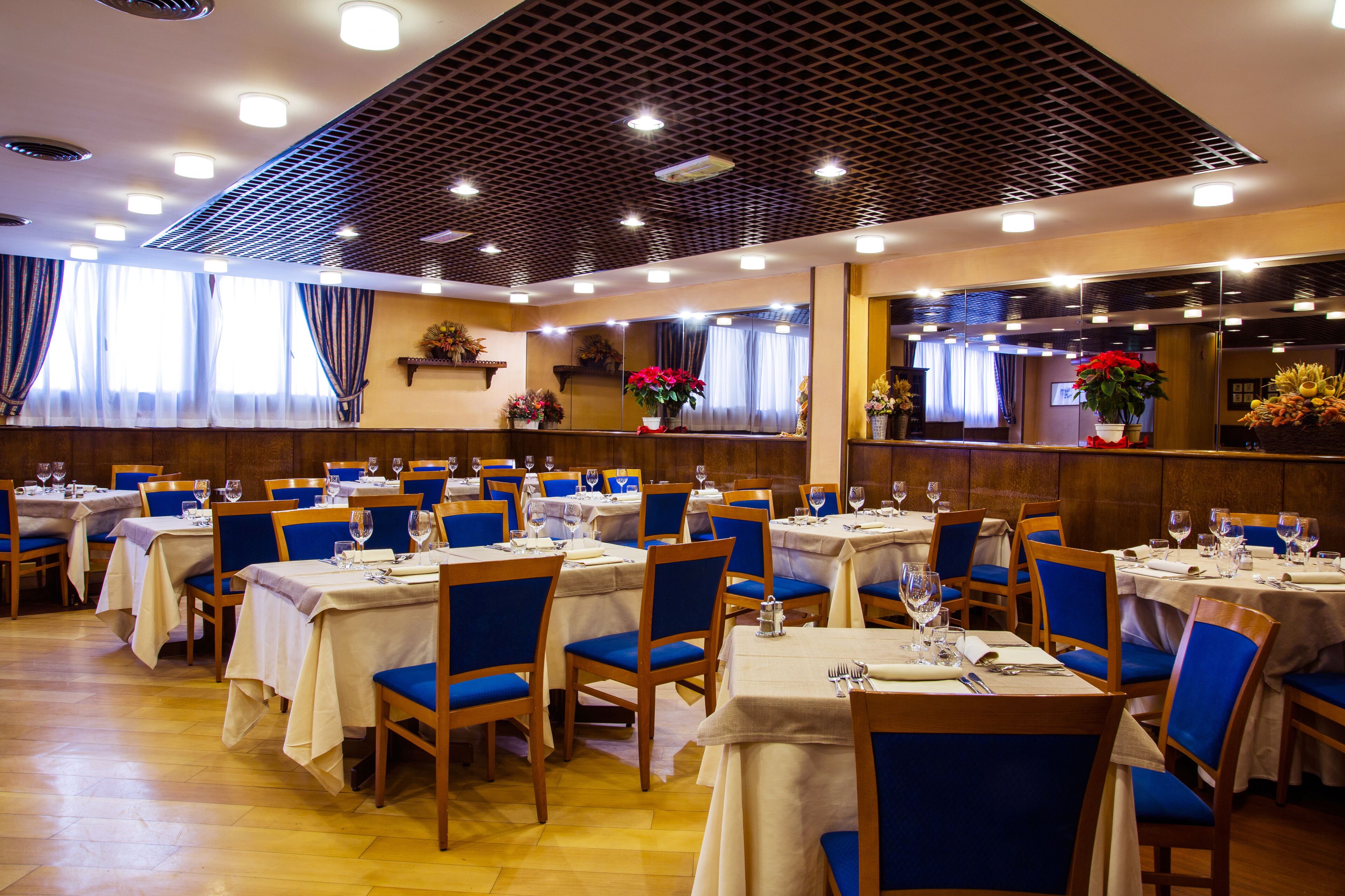 Un restaurante con varias mesas y sillas, dispuesto en un espacio amplio con suelo y techo de madera.