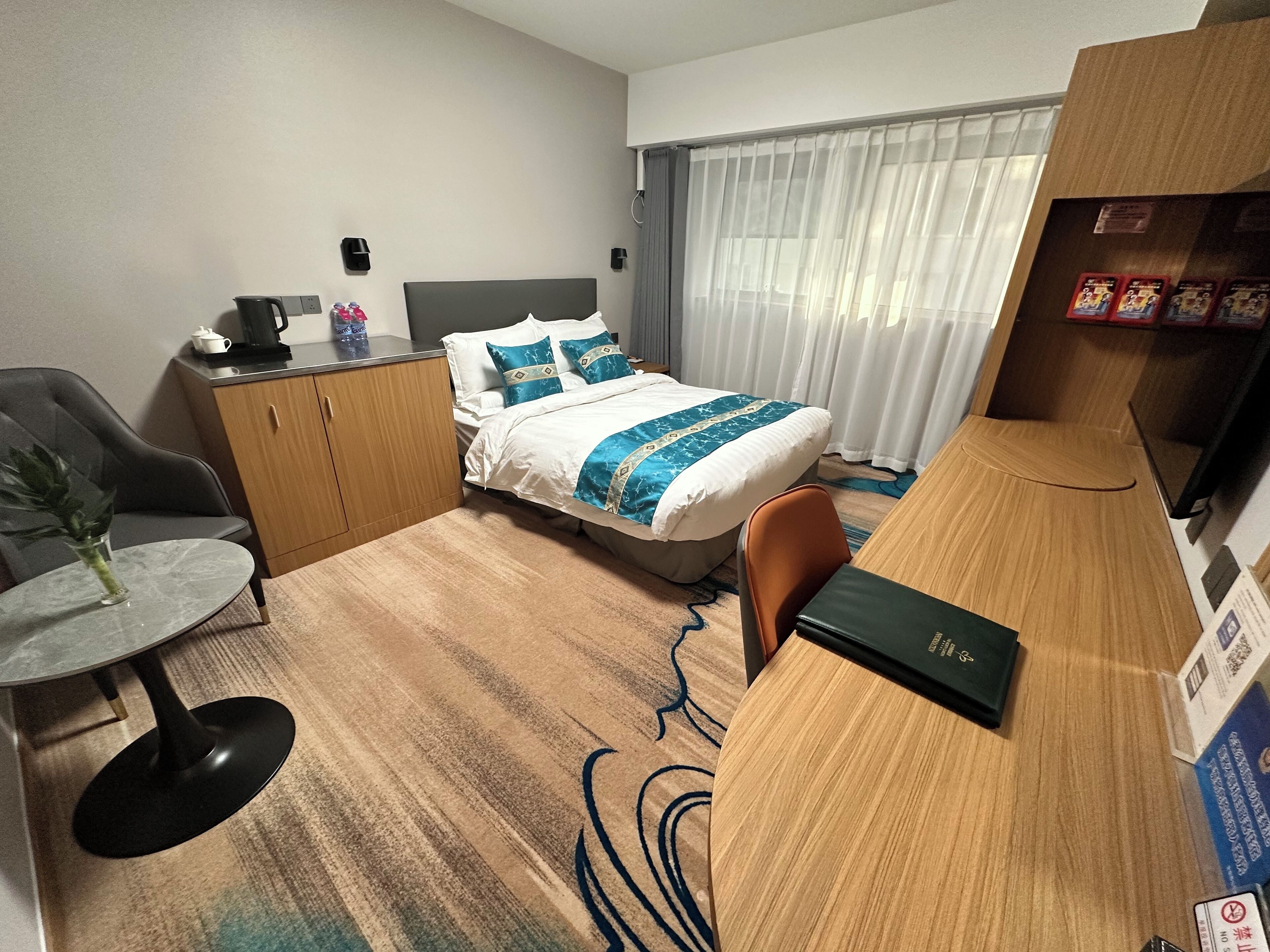 Une chambre d’hôtel comprenant un lit, un bureau, une chaise, une petite table avec un vase et un placard.