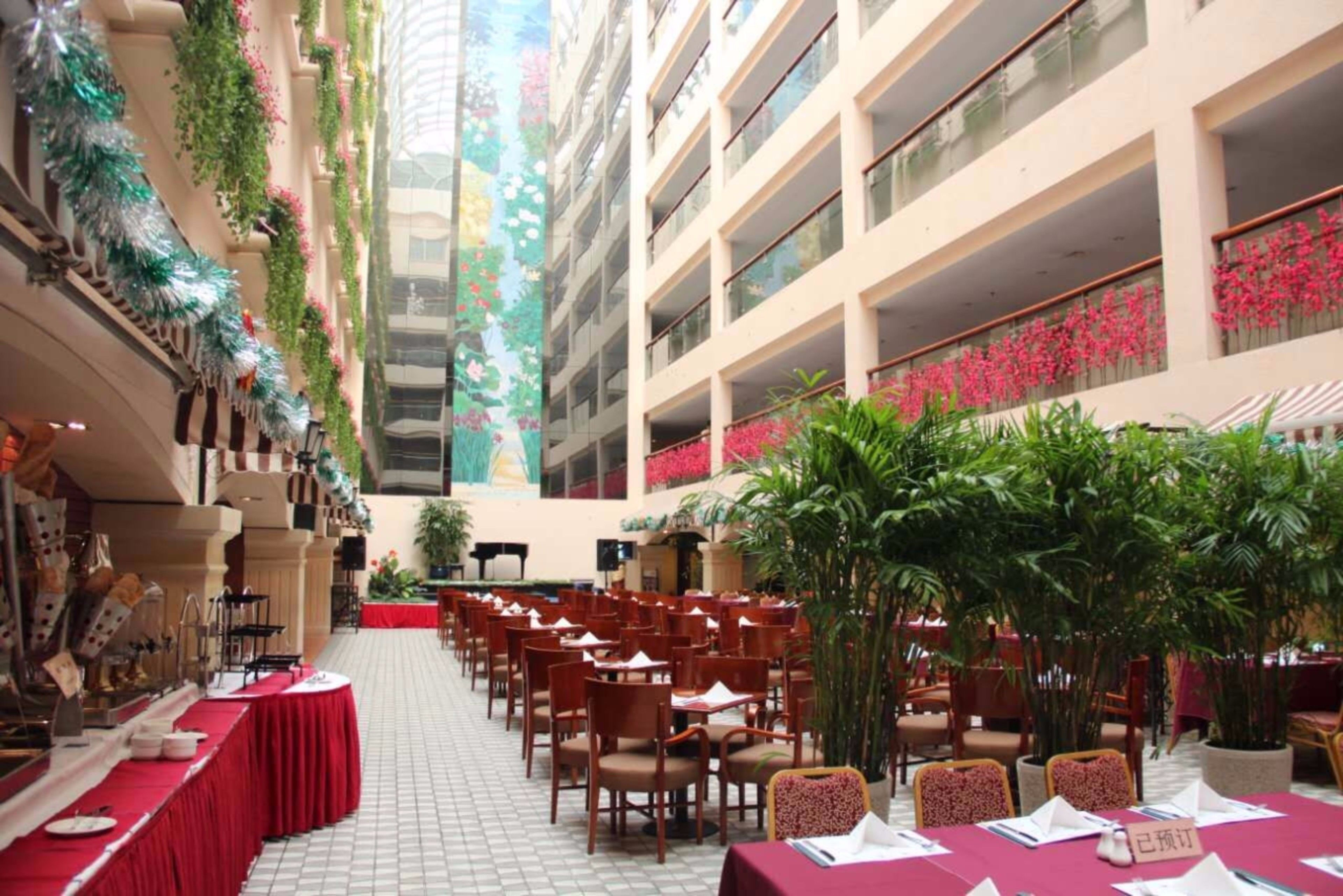 Un amplio comedor interior con varias mesas y sillas, rodeado de balcones con plantas y flores.
