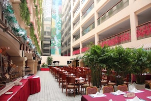 A spacious indoor dining area with multiple tables and chairs, surrounded by balconies with plants and flowers. - The North Garden Hotel Beijing Wangfujing (Beijing)