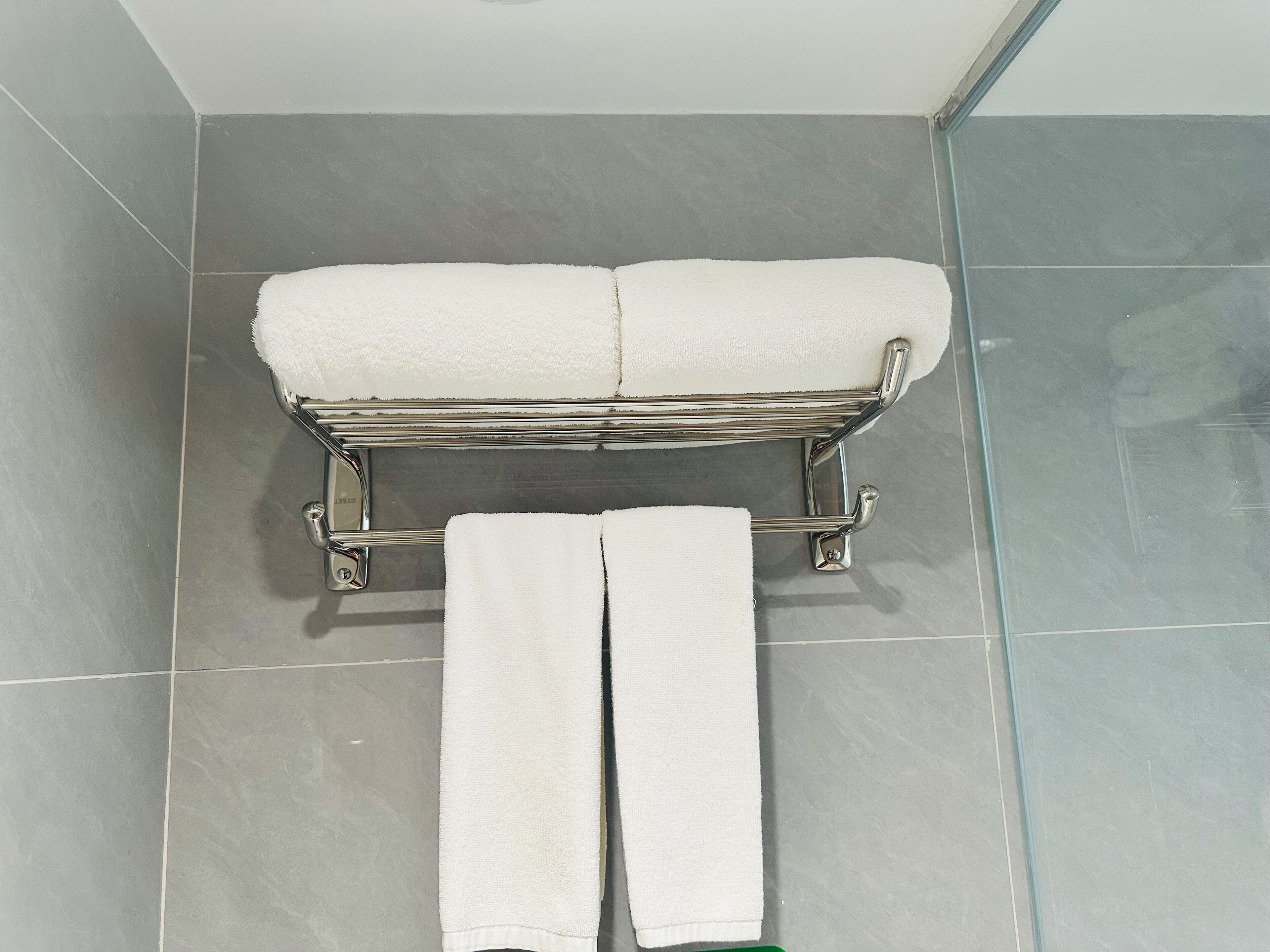A bathroom with a chrome towel rack holding two white towels and a folded towel on the floor.
