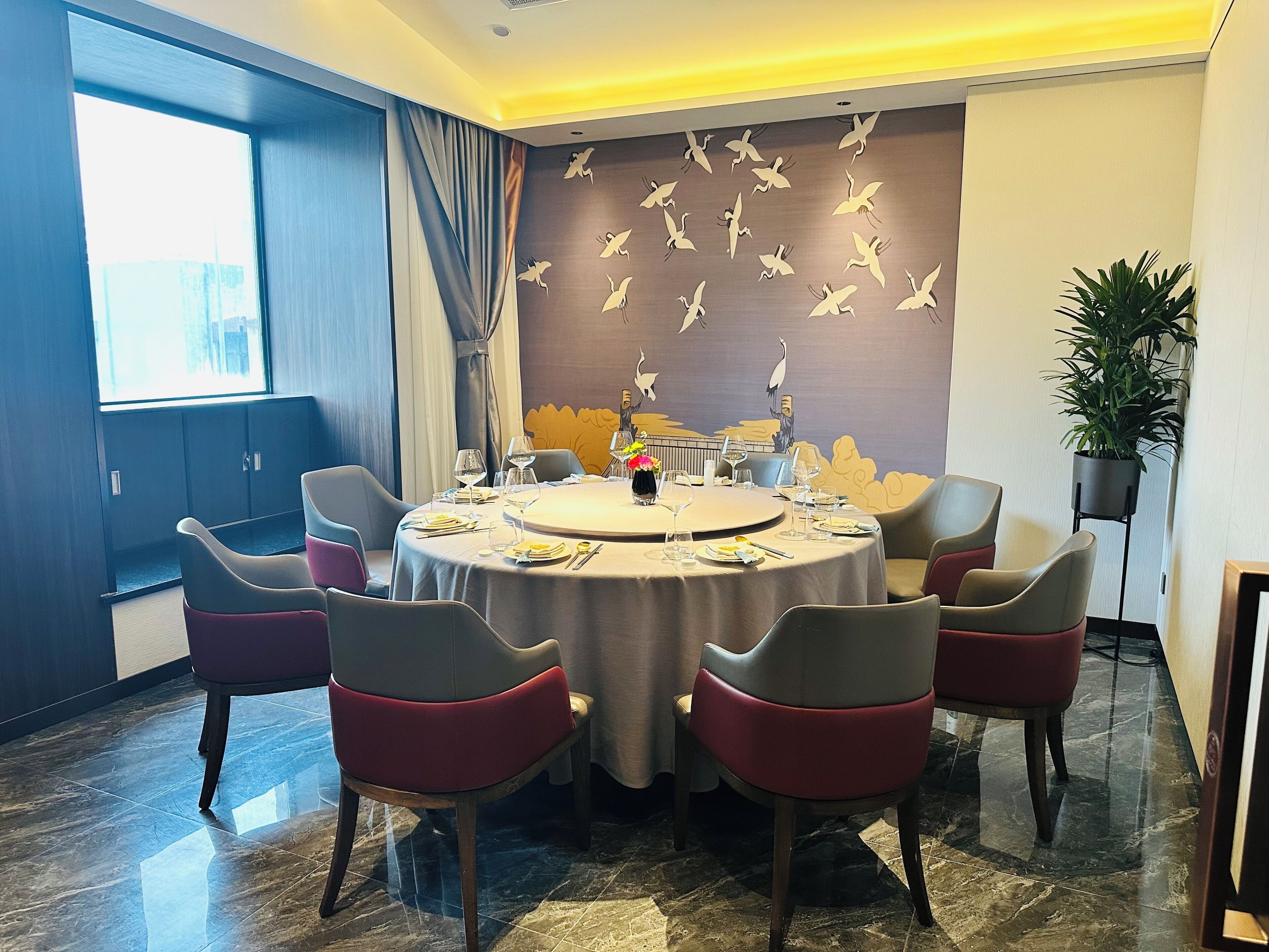 A dining area with a round table, six chairs, and a wall mural of birds.