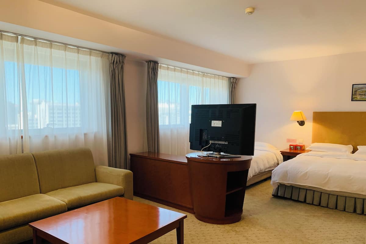 A hotel room with a sofa, a wooden desk with a television, a bed, and a nightstand with a lamp.