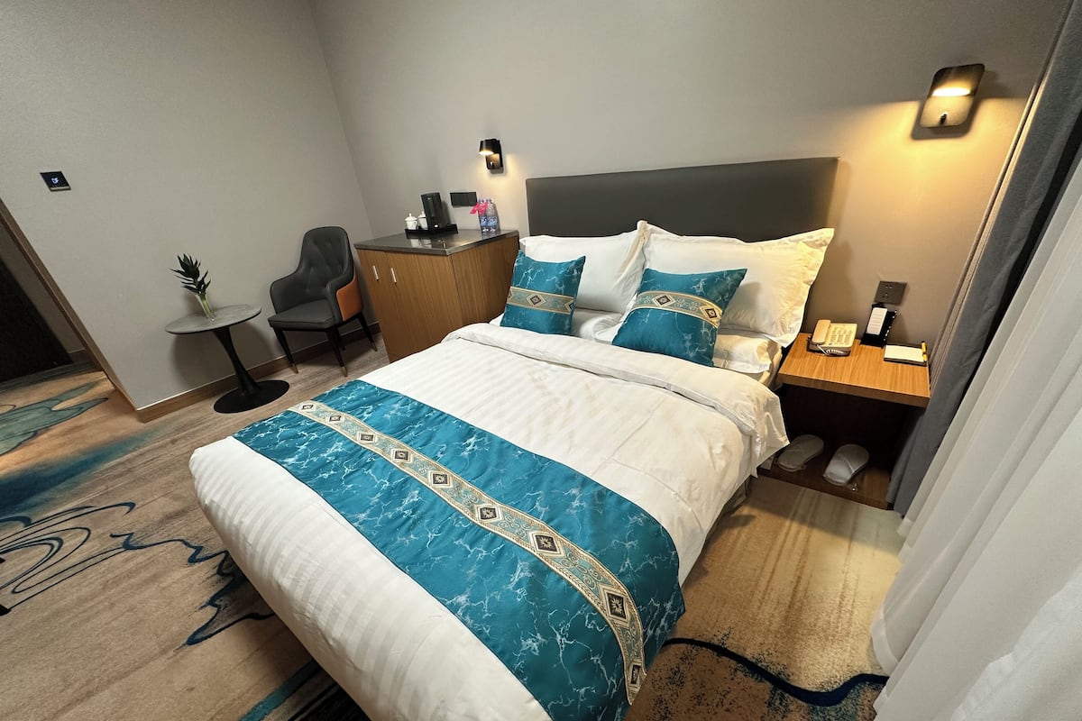 A hotel room with a bed, bedside table, chair, desk, and a small table with a plant.