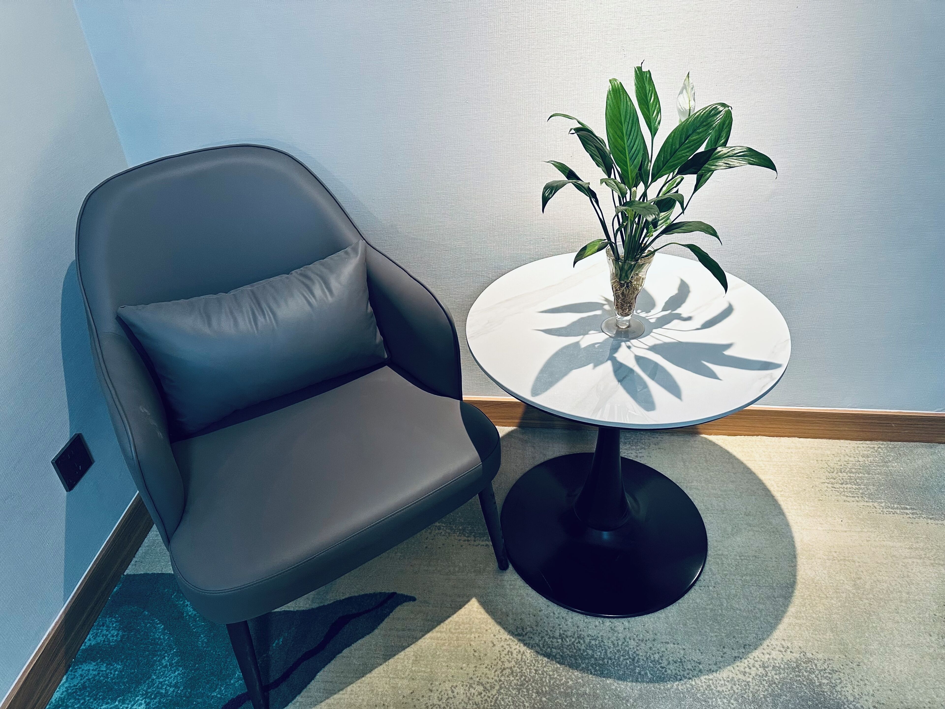 A modern room with a grey leather chair, a small round table with a plant, and a textured wall.