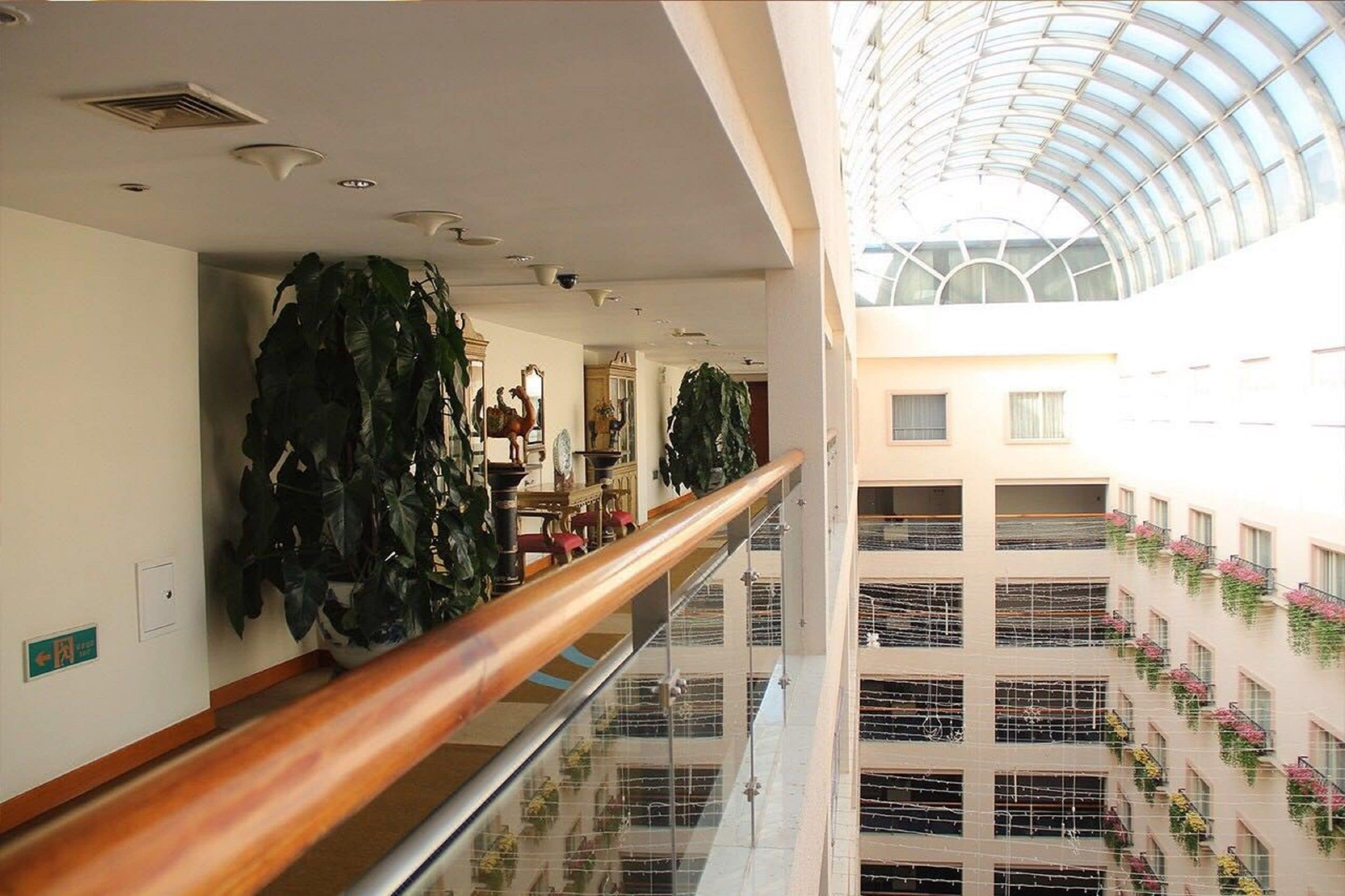 A multi-level atrium with a glass ceiling, wooden railings, and potted plants.