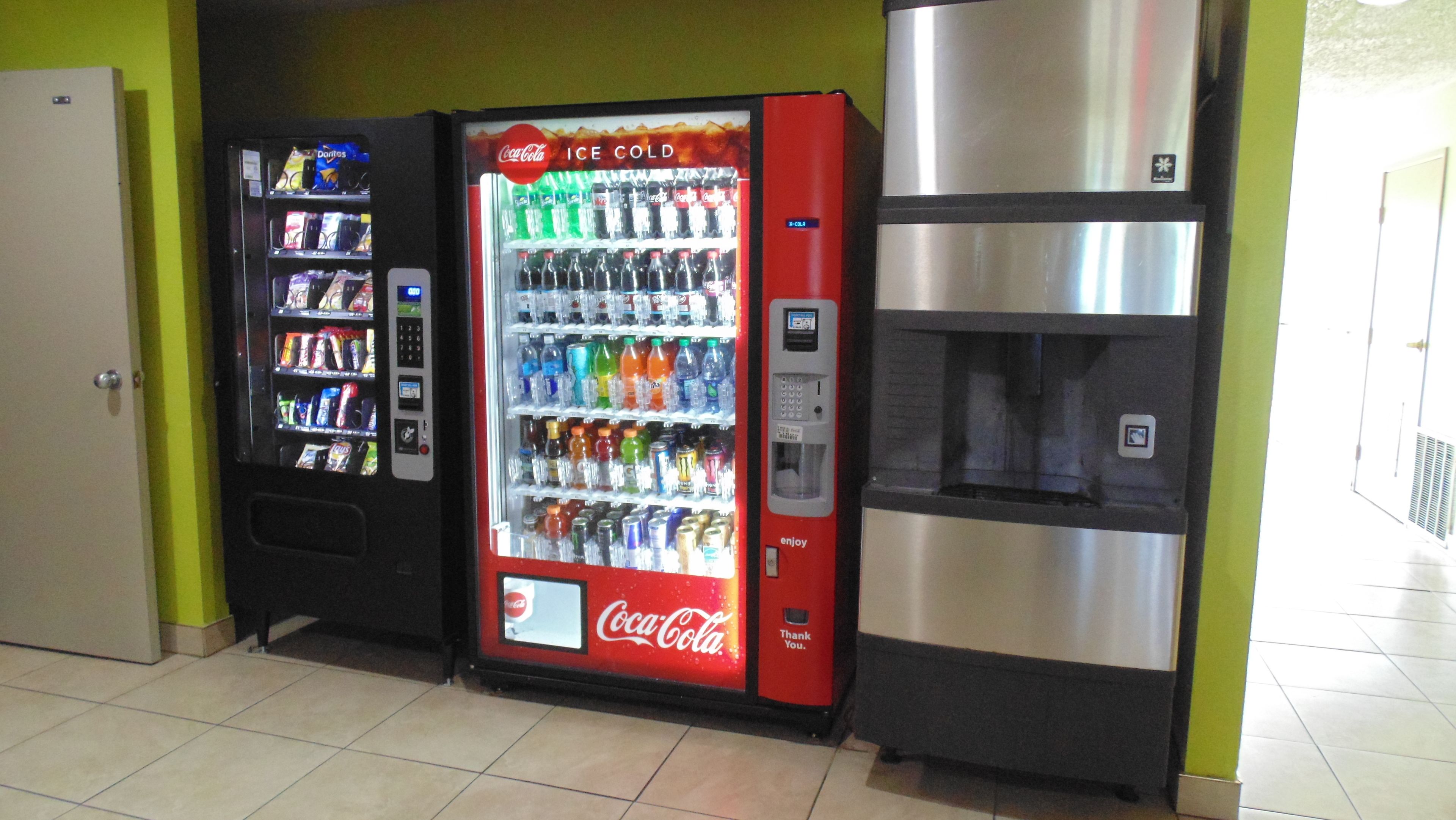 A vending machine area with a Coca-Cola Ice Cold machine and a Doritos machine, and a stainless steel refrigerator.