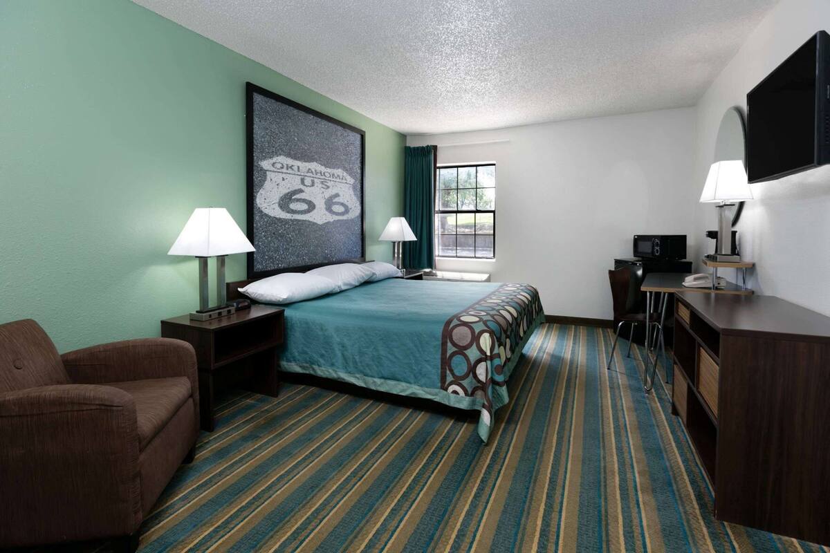 A hotel room with a bed, two bedside lamps, a desk with a computer, a TV, and a chair.