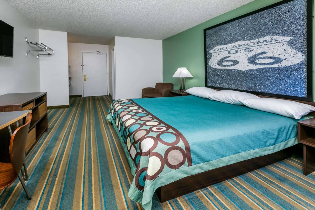 A hotel room with a bed, a desk, a chair, a lamp, and a wall-mounted TV.