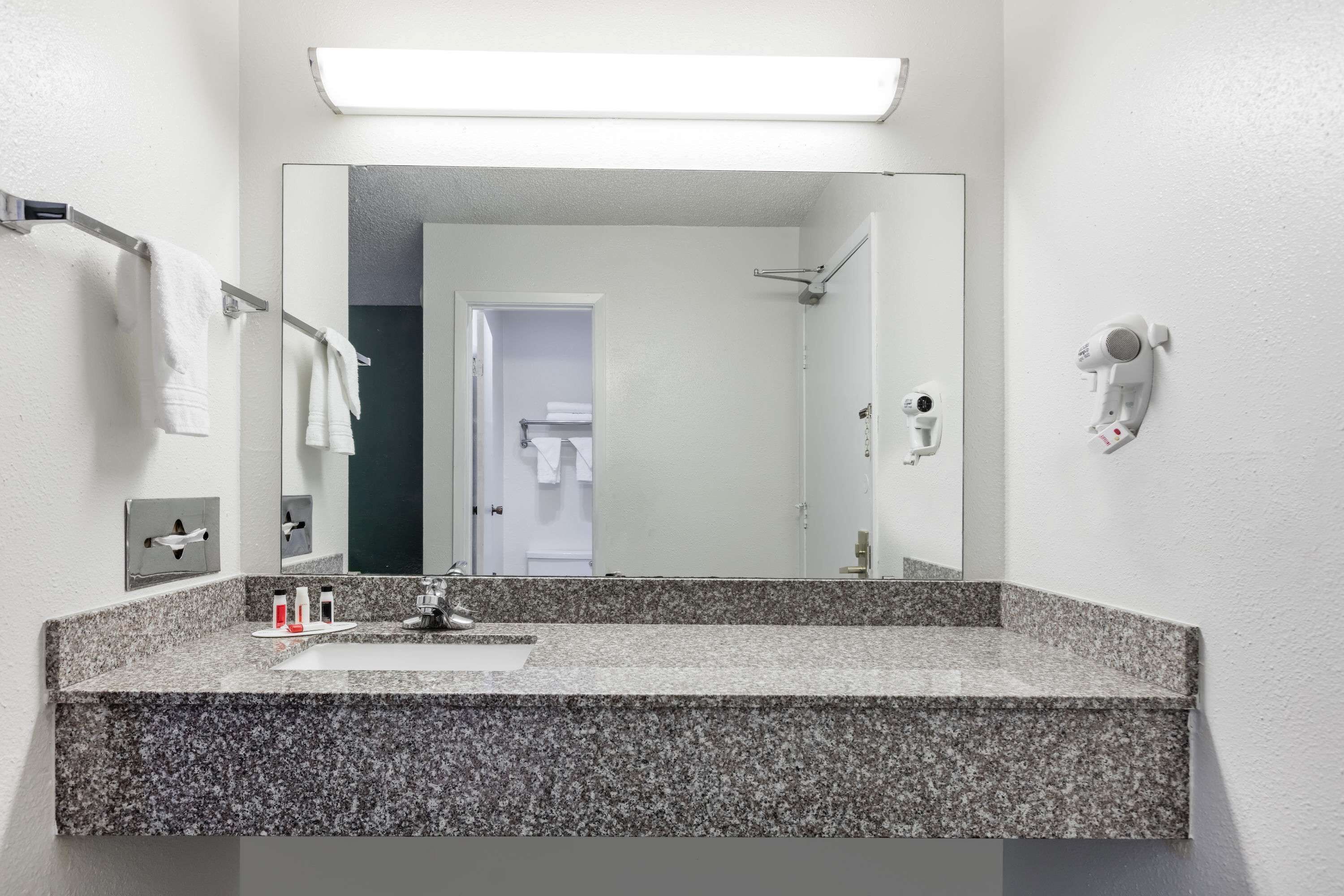 A modern bathroom with a granite countertop sink, a large mirror, and a hairdryer mounted on the wall.
