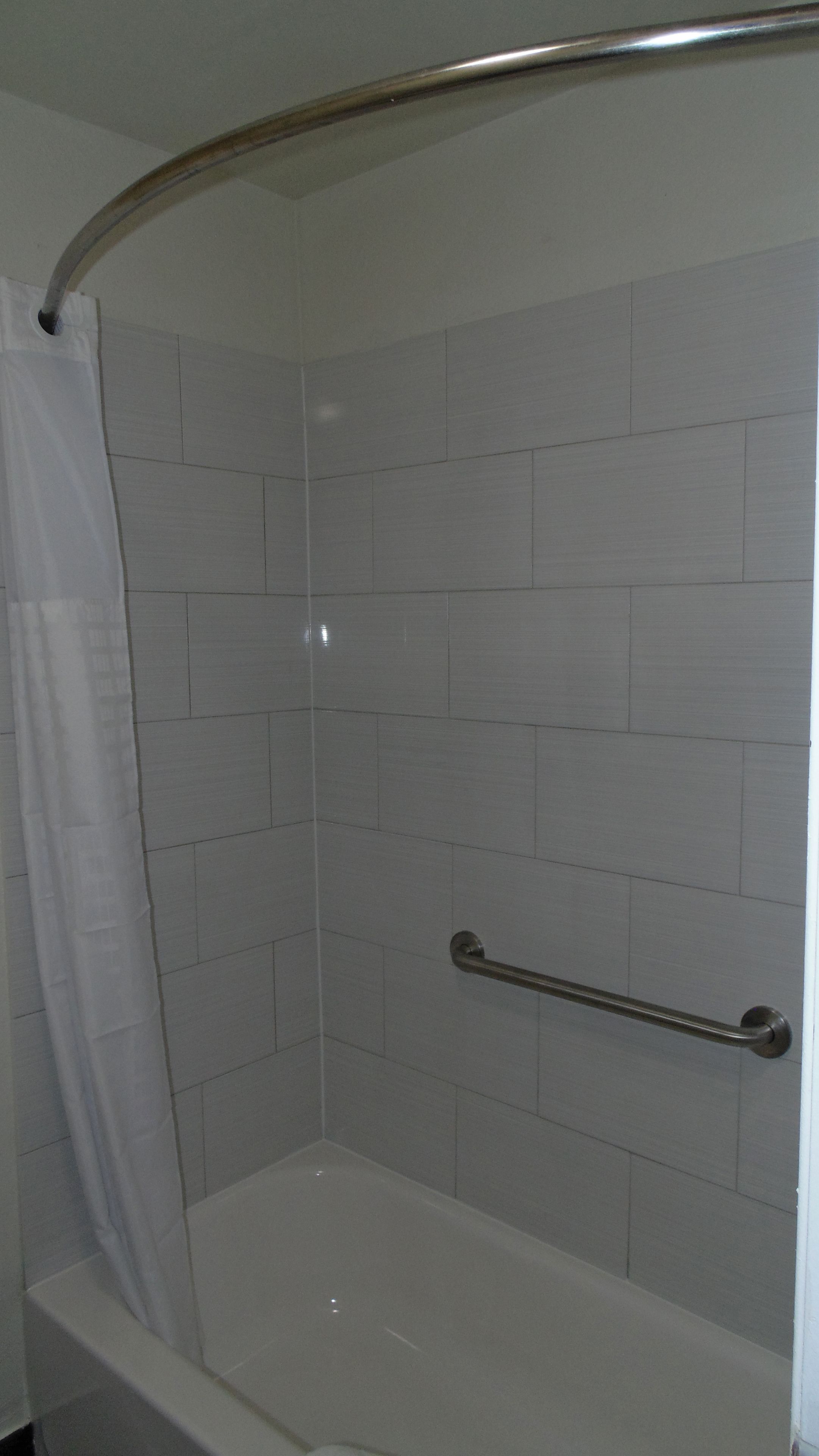 A bathroom with white tiled walls, a white bathtub, and a shower area with a metal grab bar.