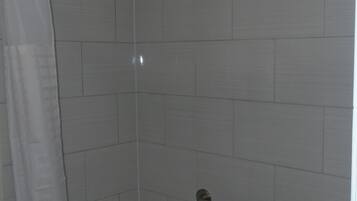 A bathroom with white tiled walls, a white bathtub, and a shower area with a metal grab bar.