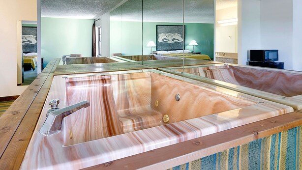 Una habitación con una bañera de madera grande, una cama frente a una pared verde y un televisor sobre un mueble.