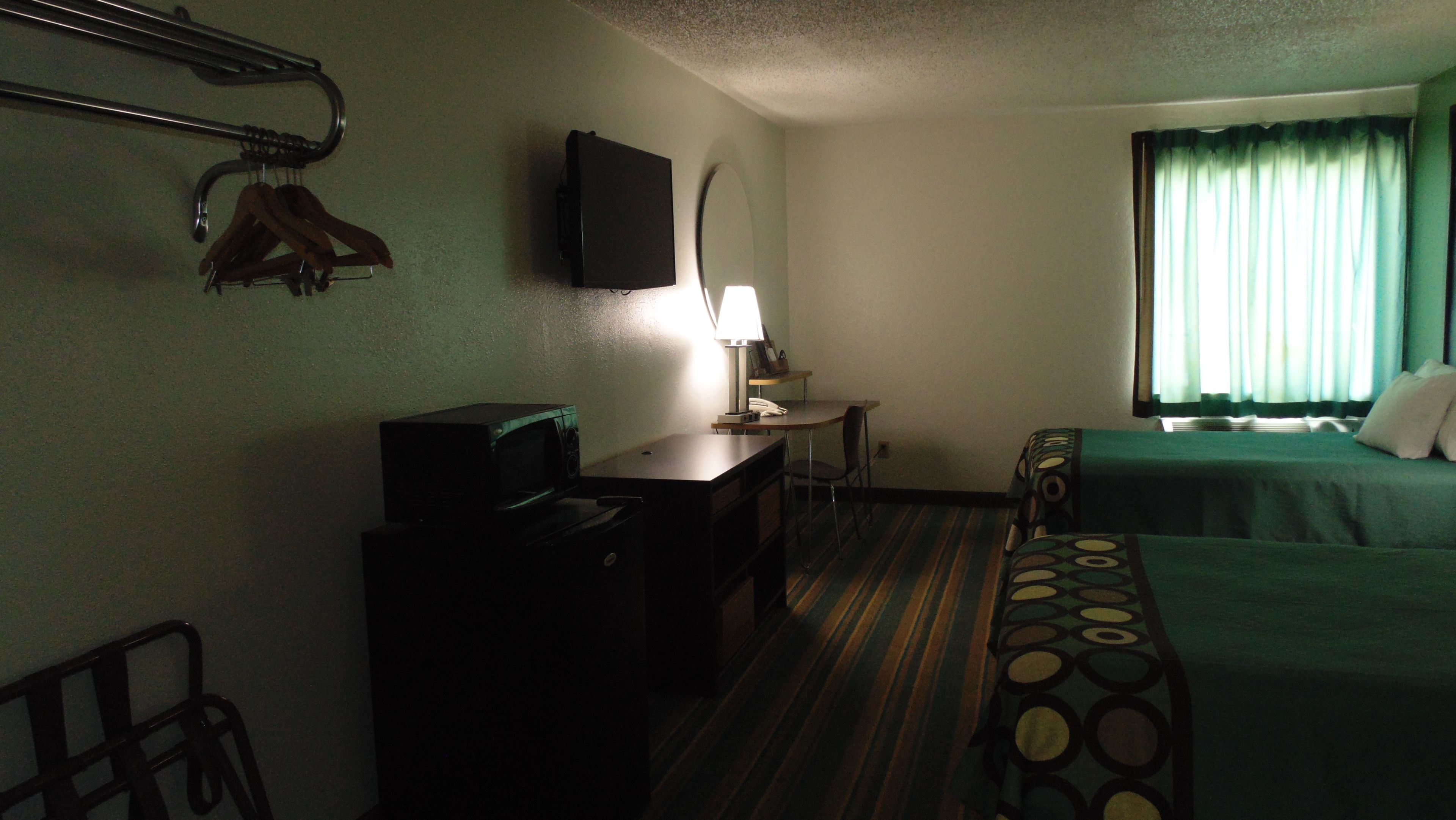 A hotel room with a bed, a desk, a chair, a TV mounted on the wall, and a window with curtains.