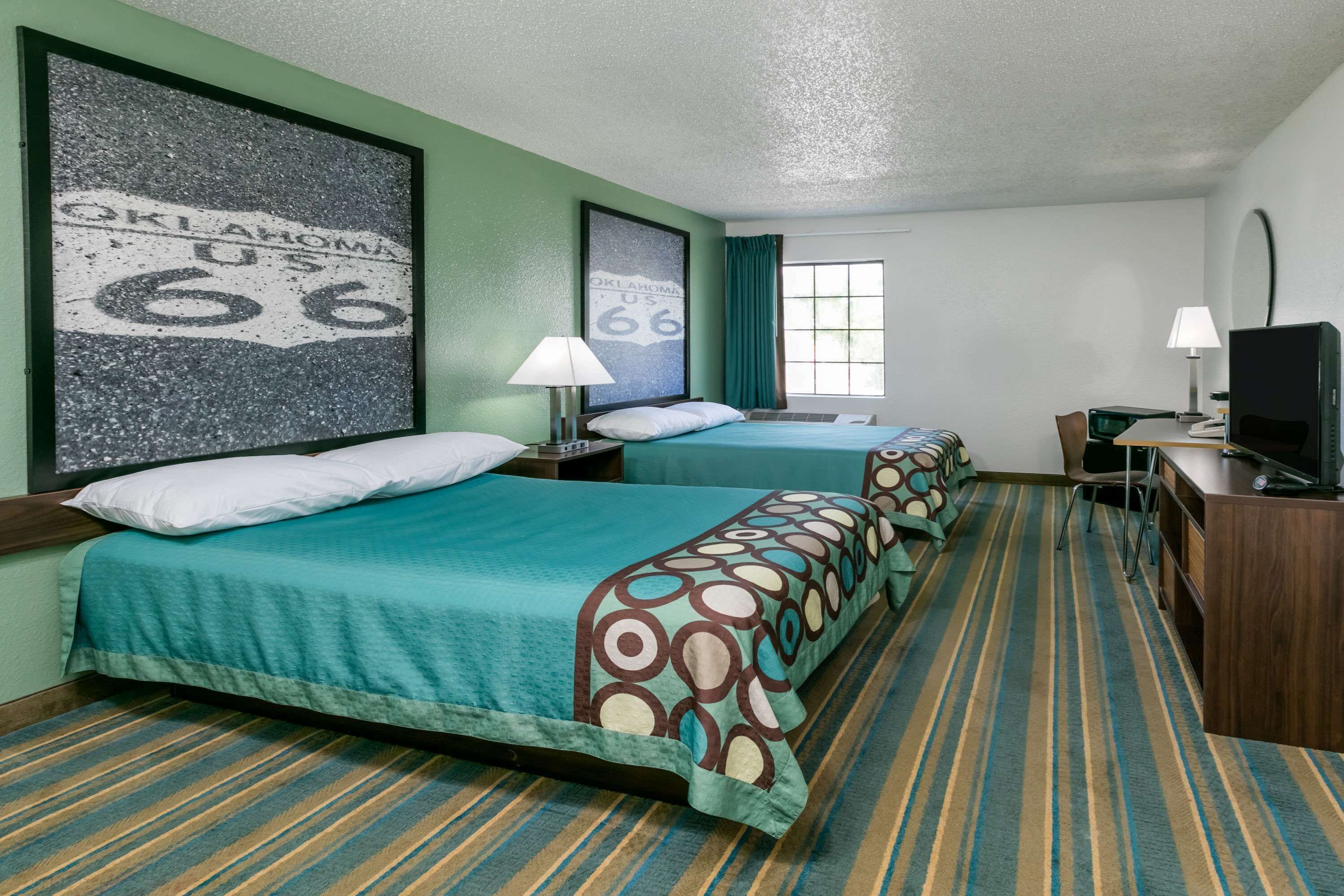 A hotel room with two beds, a desk, a TV, and a window with curtains.