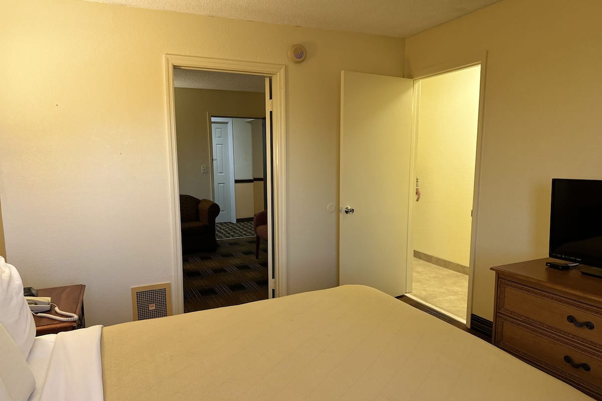 Une chambre d’hôtel comprenant un lit, une commode, un téléviseur et une porte donnant sur un couloir où se trouvent une chaise et une autre porte.