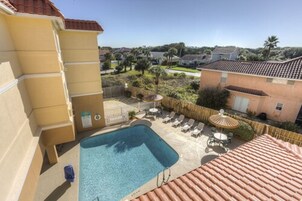 Un área de piscina con una piscina rectangular, sillas de descanso y una mesa pequeña con sombrilla.