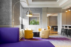 A modern hotel room with a purple sofa, yellow chairs, a black coffee table, and a large window with a view of greenery. - DoubleTree by Hilton Hotel Savannah Historic District (Savannah)
