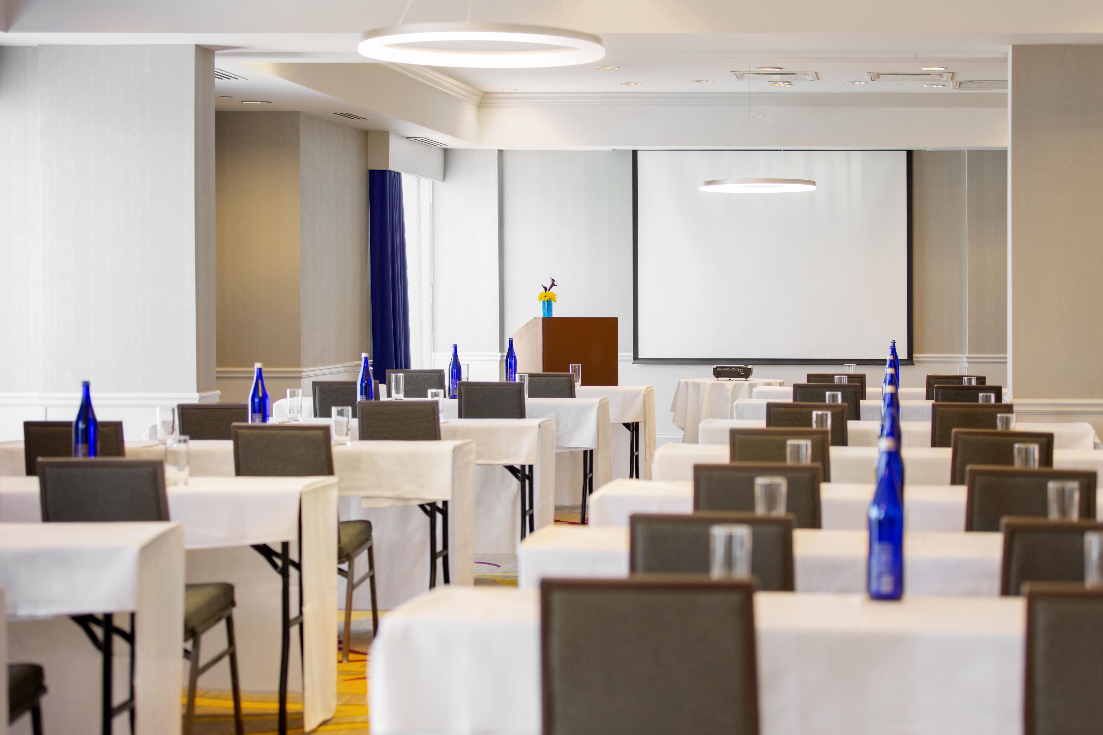 A conference room with rows of tables, chairs, and a projector screen.