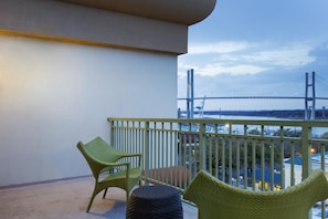 A balcony with two wicker chairs and a round ottoman, overlooking a bridge and a body of water. - DoubleTree by Hilton Hotel Savannah Historic District (Savannah)