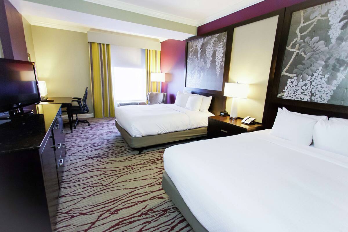 A hotel room with two beds, a desk with a TV, a chair, and a large painting on the wall.