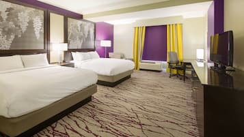 A hotel room with two beds, a desk, a TV, and a large window with curtains.