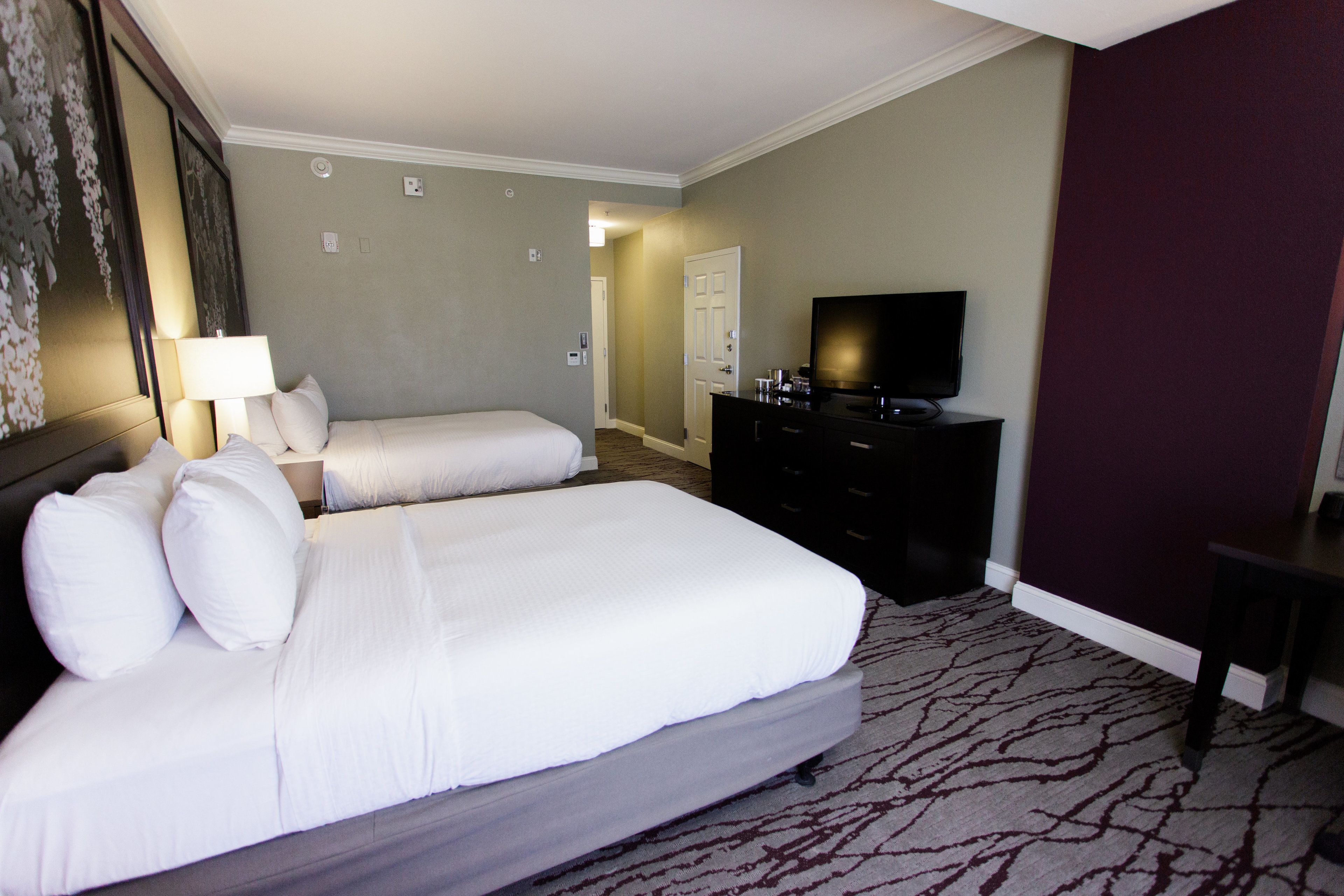 A hotel room with two beds, a television, a dresser, and a door leading to another room.