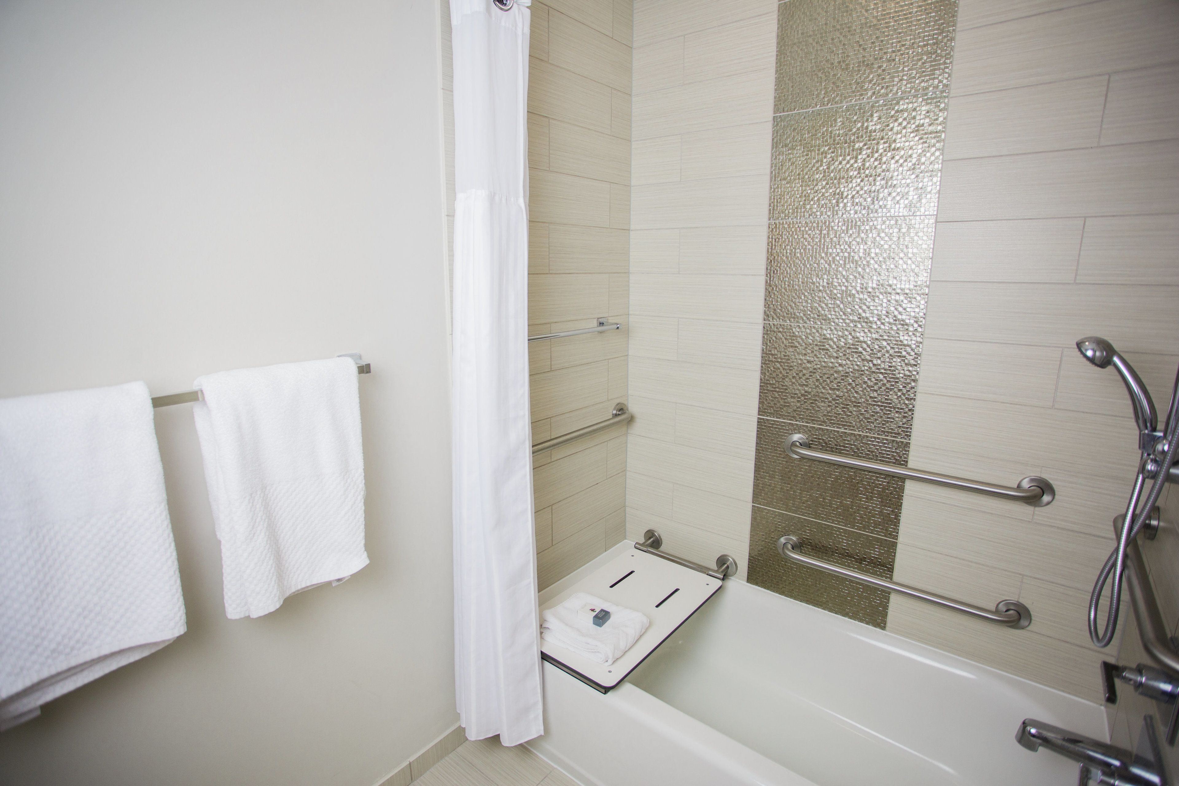 A modern bathroom with a bathtub, a shower with a glass door, and a towel rack with two white towels.