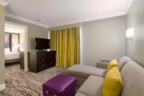 A hotel room with a bed, a TV, a sofa, a small table, and a suitcase. - DoubleTree by Hilton Hotel Savannah Historic District (Savannah)