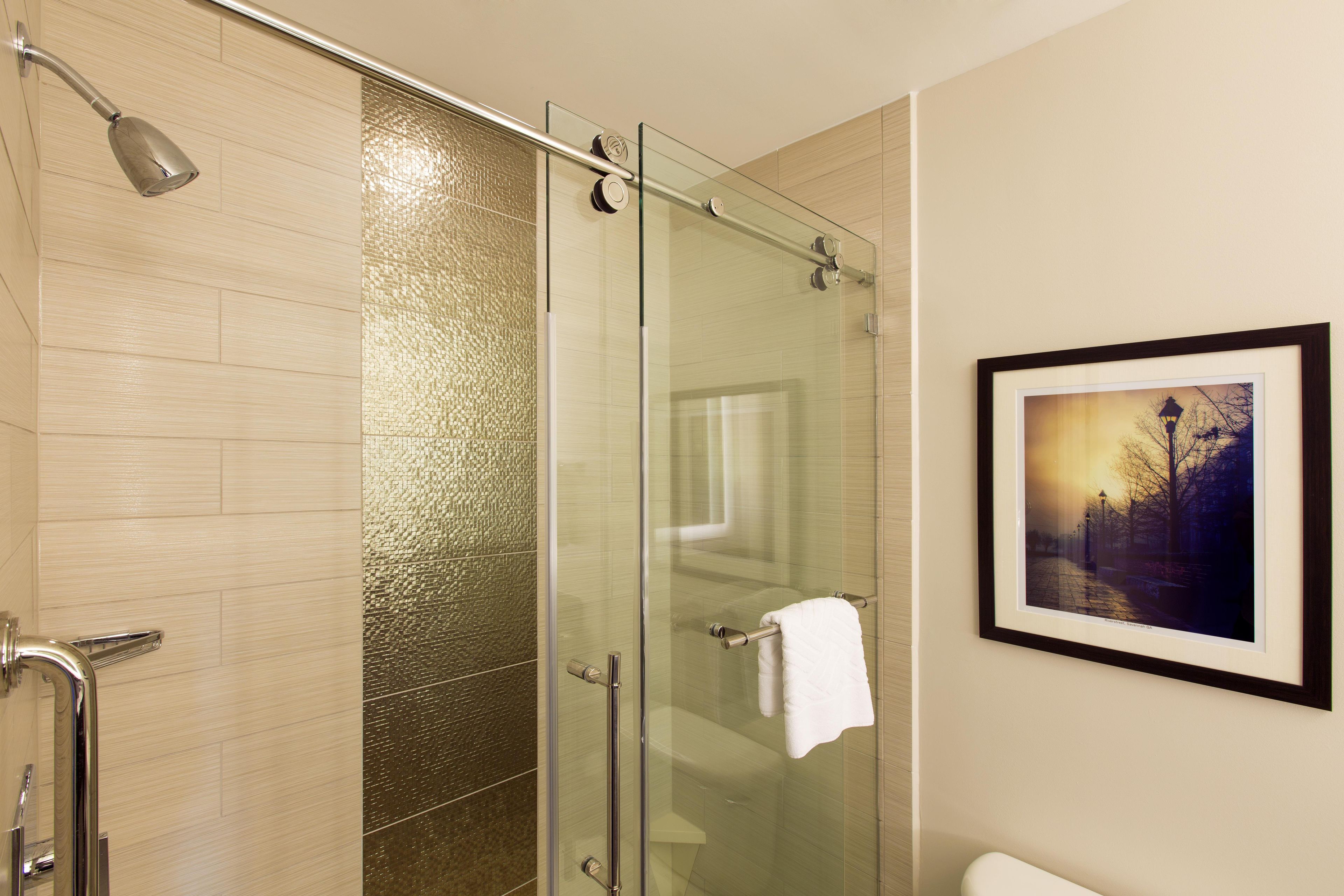 A modern bathroom with a glass shower enclosure, a framed picture on the wall, and a towel hanging on the shower door handle.