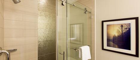 A modern bathroom with a glass shower enclosure, a framed picture on the wall, and a towel hanging on the shower door handle.