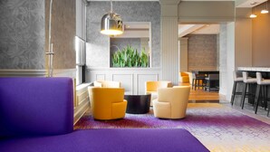 A modern lobby with a purple sofa, yellow chairs, a black coffee table, and a large mirror. - DoubleTree by Hilton Hotel Savannah Historic District (Savannah)