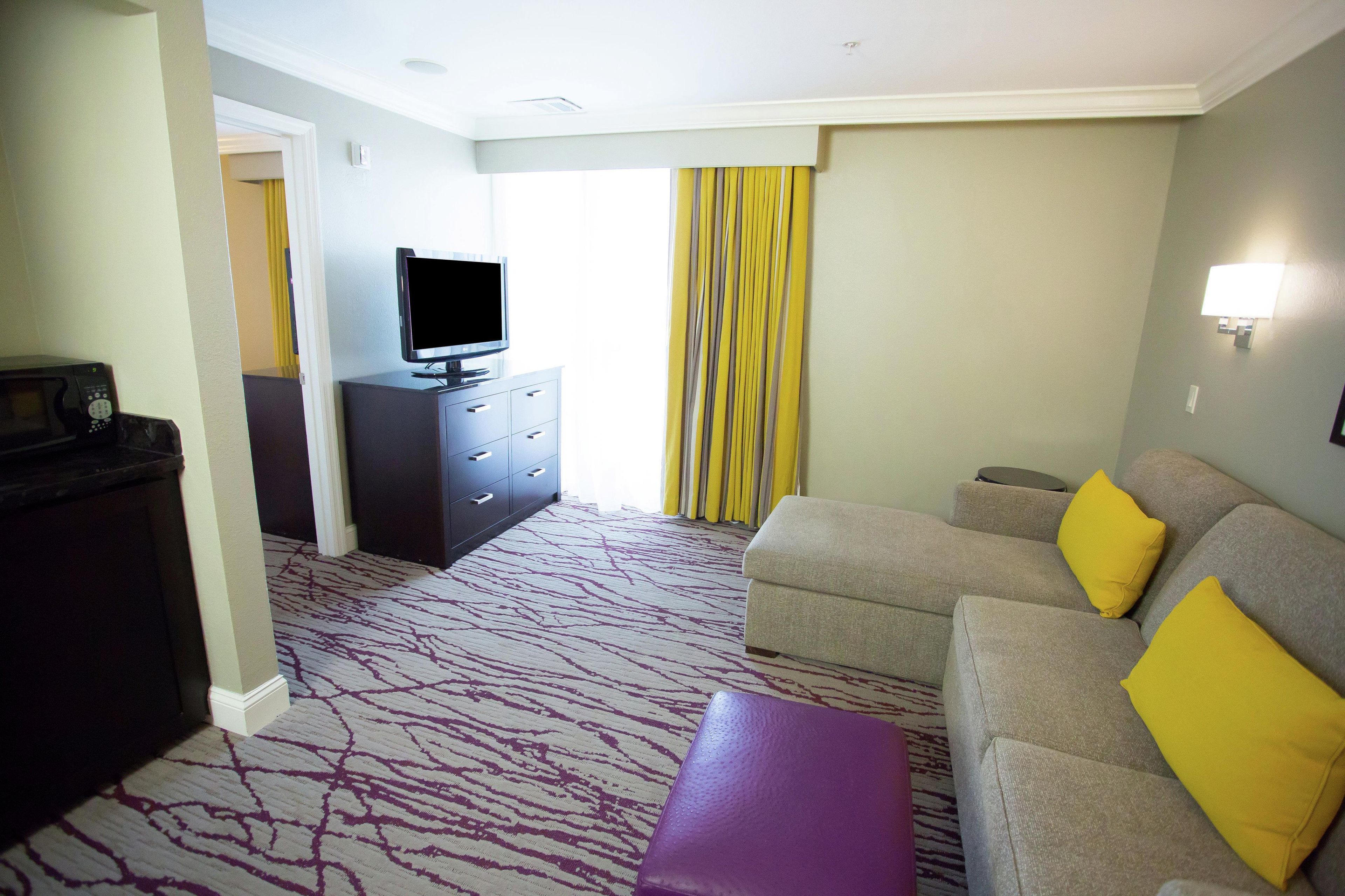 A hotel room with a sofa, a television, a small table, a dark-colored cabinet, and a patterned carpet.