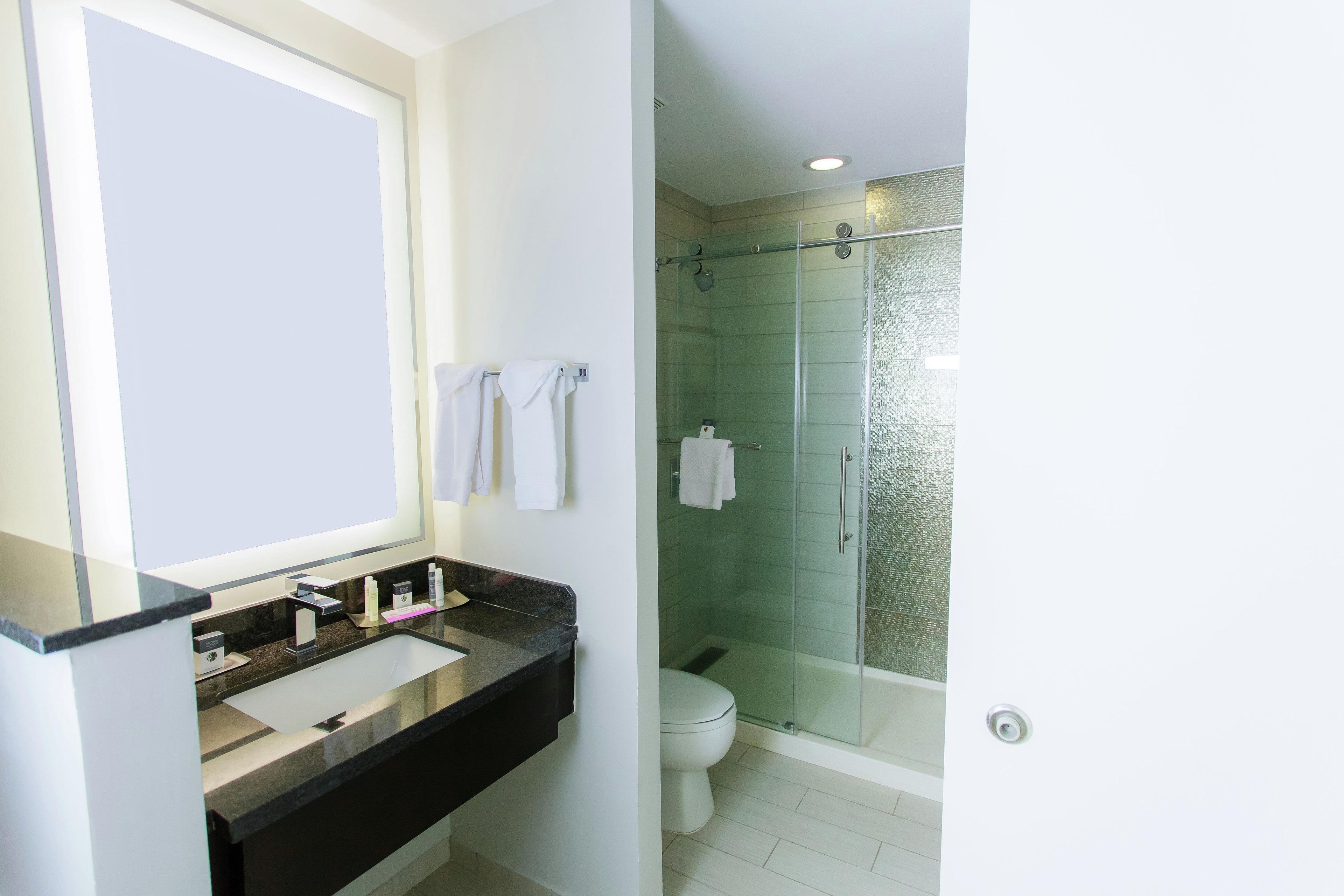 Un baño con ducha envuelta en vidrio, inodoro blanco y tocador con espejo y lavabo.