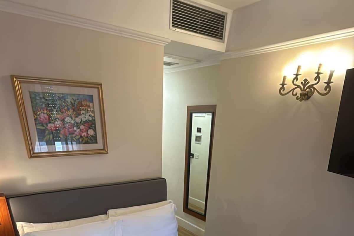 A hotel room with a large bed, a nightstand, a wall-mounted TV, a painting, and a wall-mounted light fixture.
