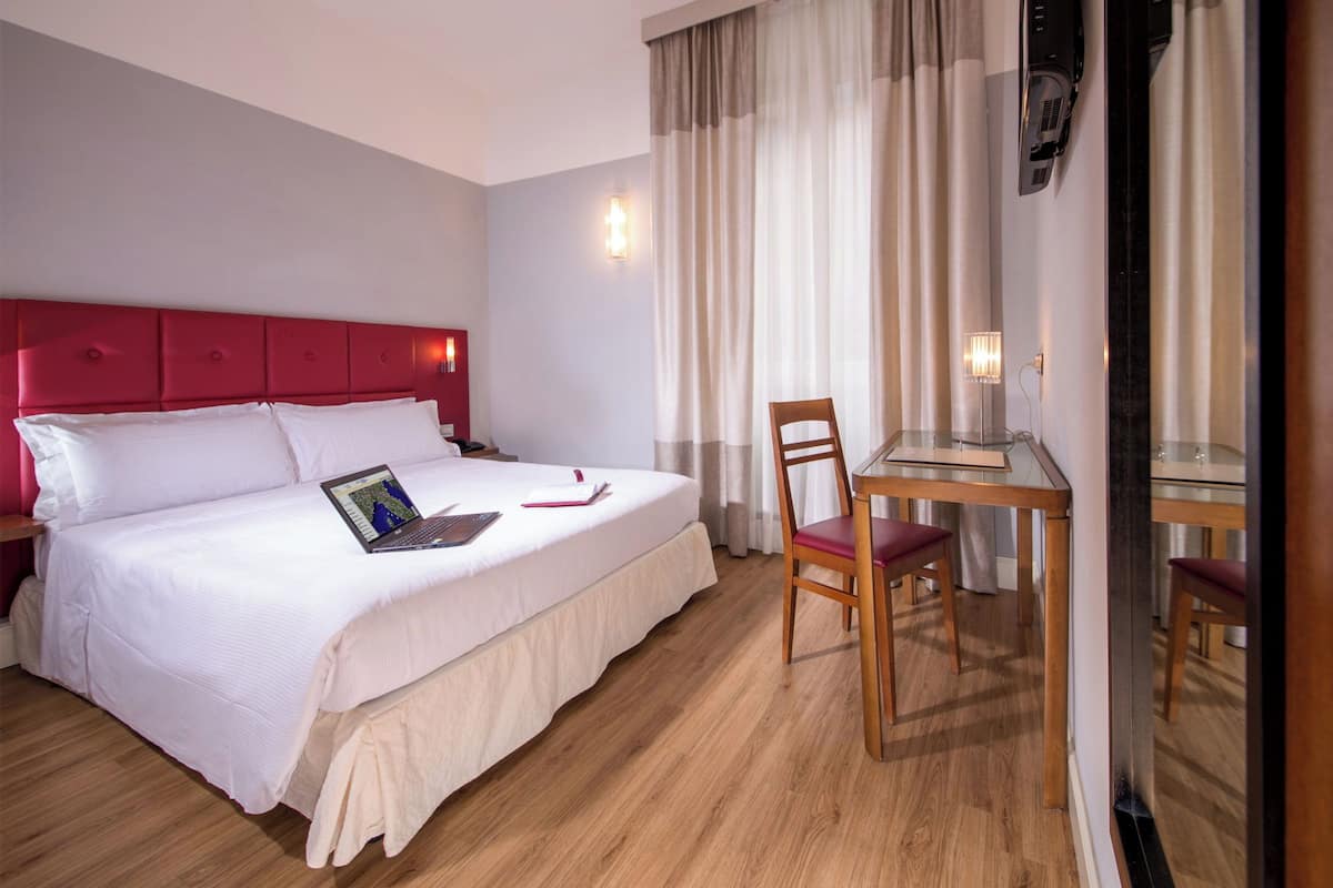 A hotel room with a bed, a desk, and a chair.