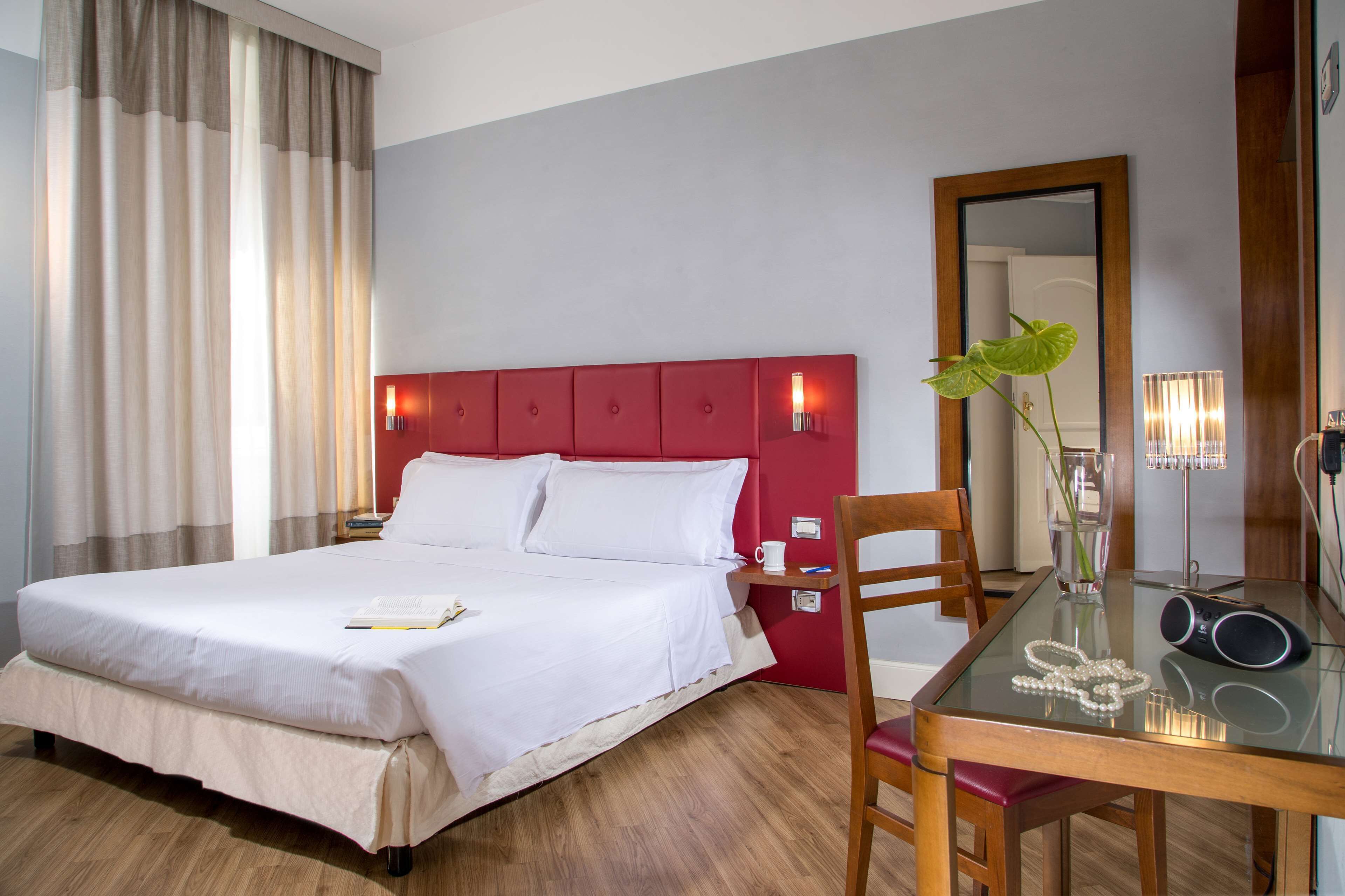 A hotel room with a bed, a dining table, a chair, a mirror, and a plant.