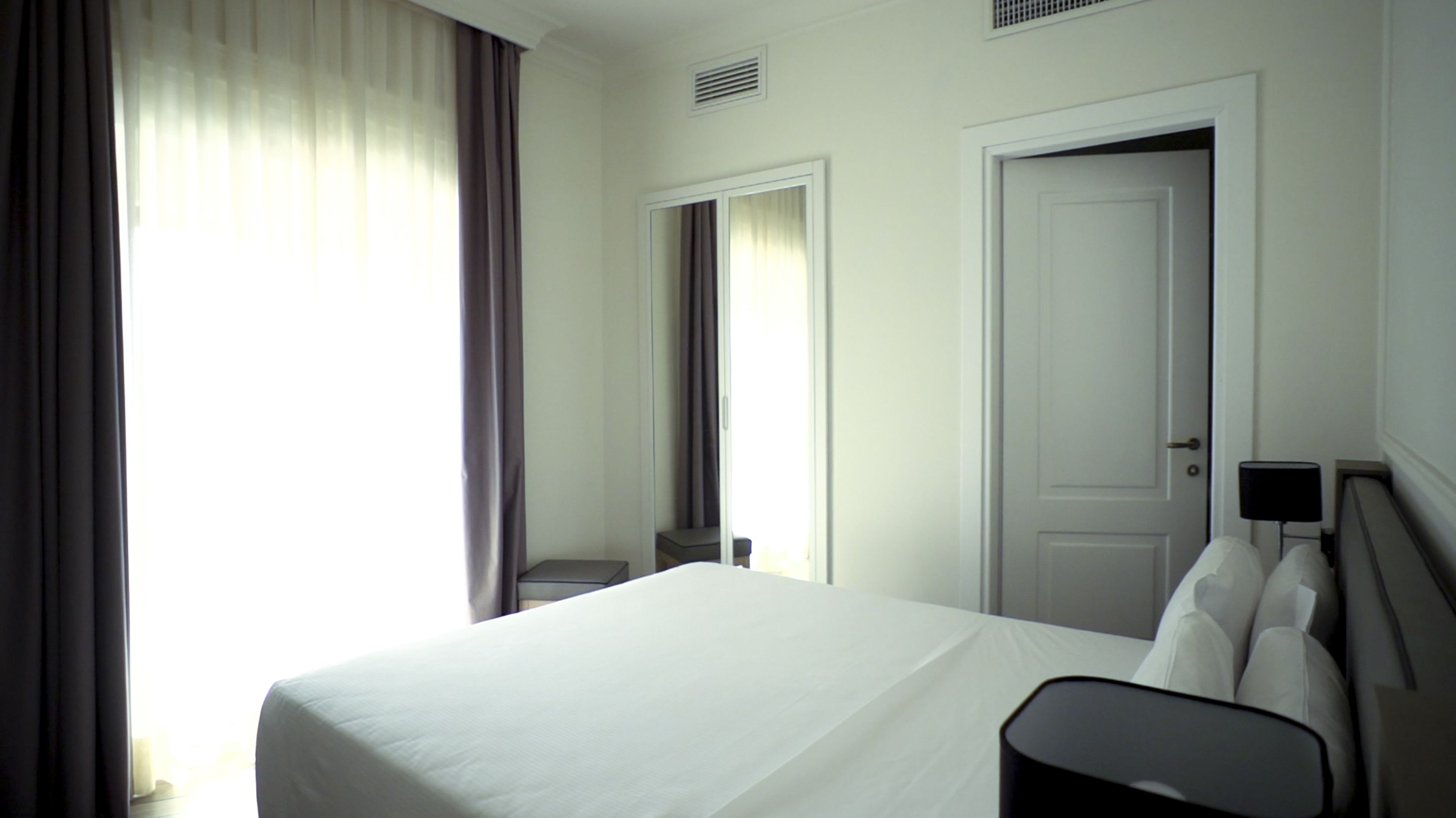 A hotel room with a large bed, a chair, a desk, and a door.