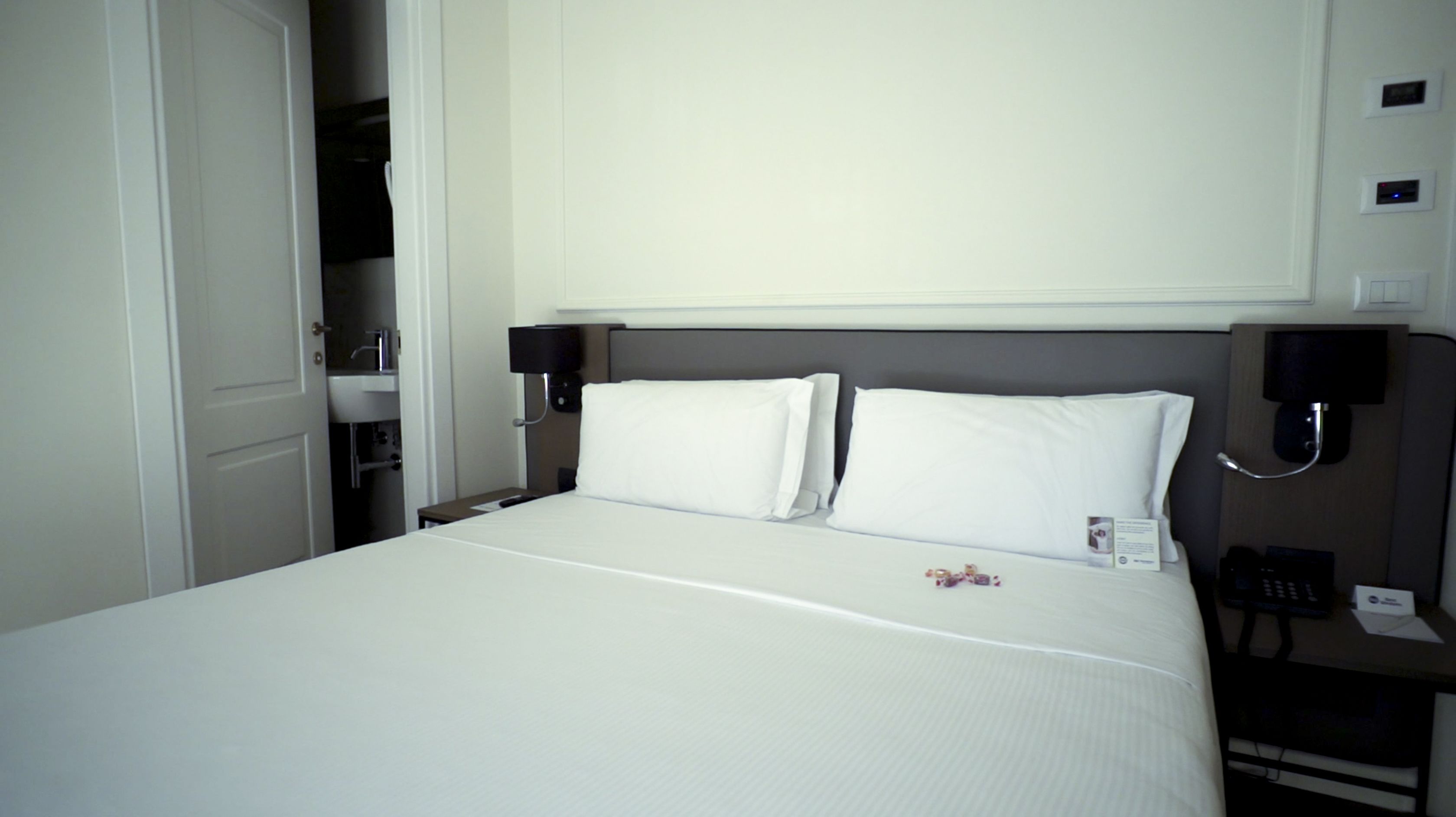 A hotel room with a large bed, two bedside tables with lamps, a bedside phone, and a small table with a remote control.
