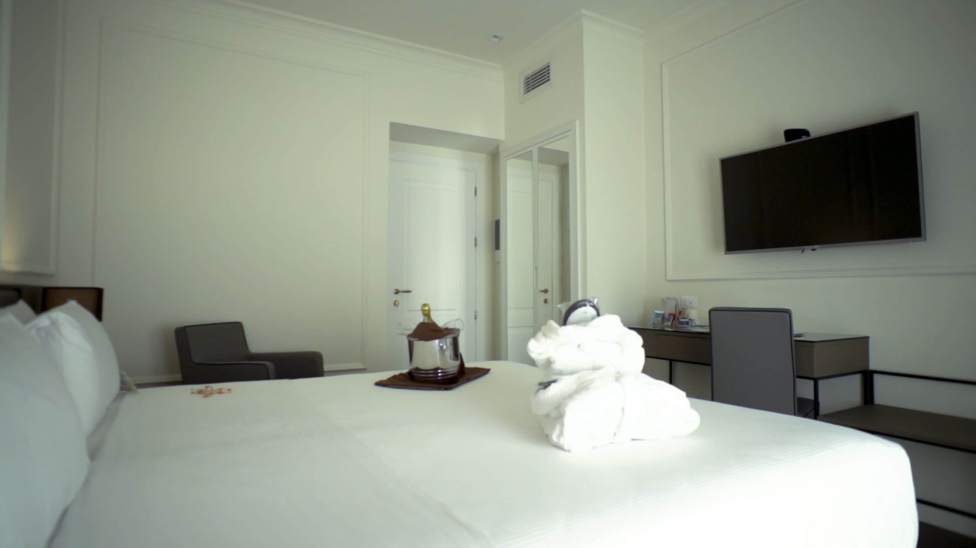 Habitación de hotel con una cama grande, televisor montado en la pared, escritorio con silla y minibar.
