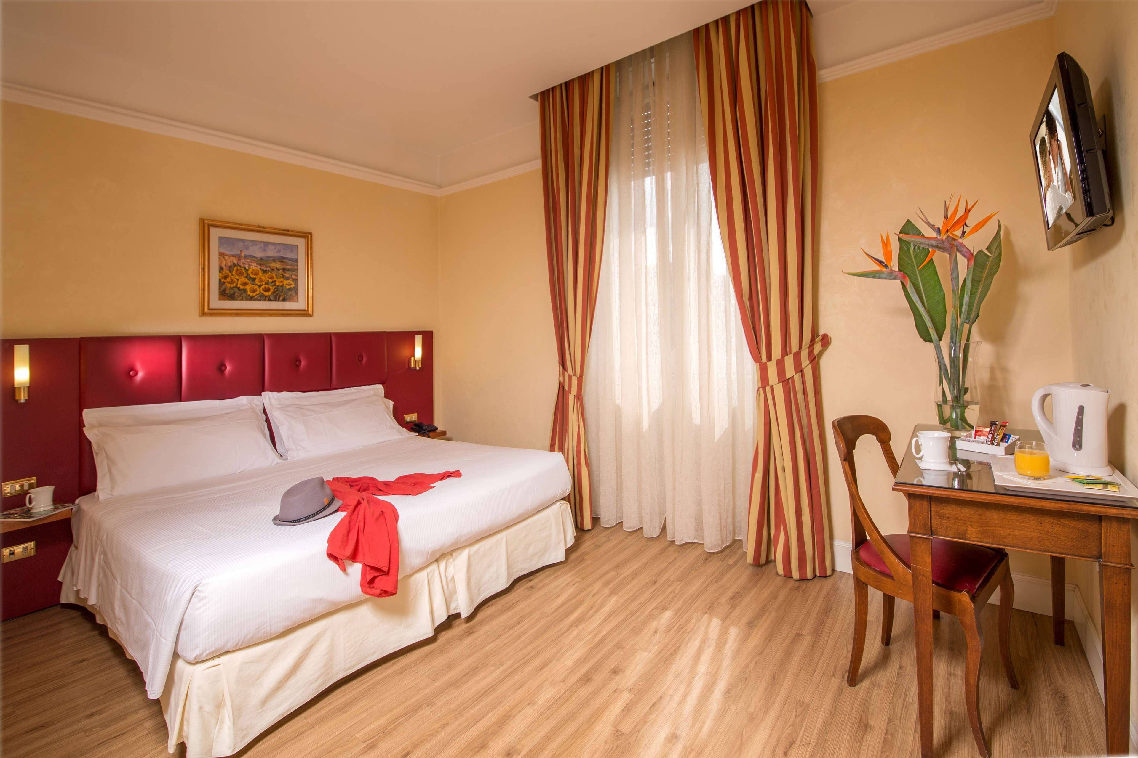 A hotel room with a bed, a desk with a chair, a television, and a window with curtains.