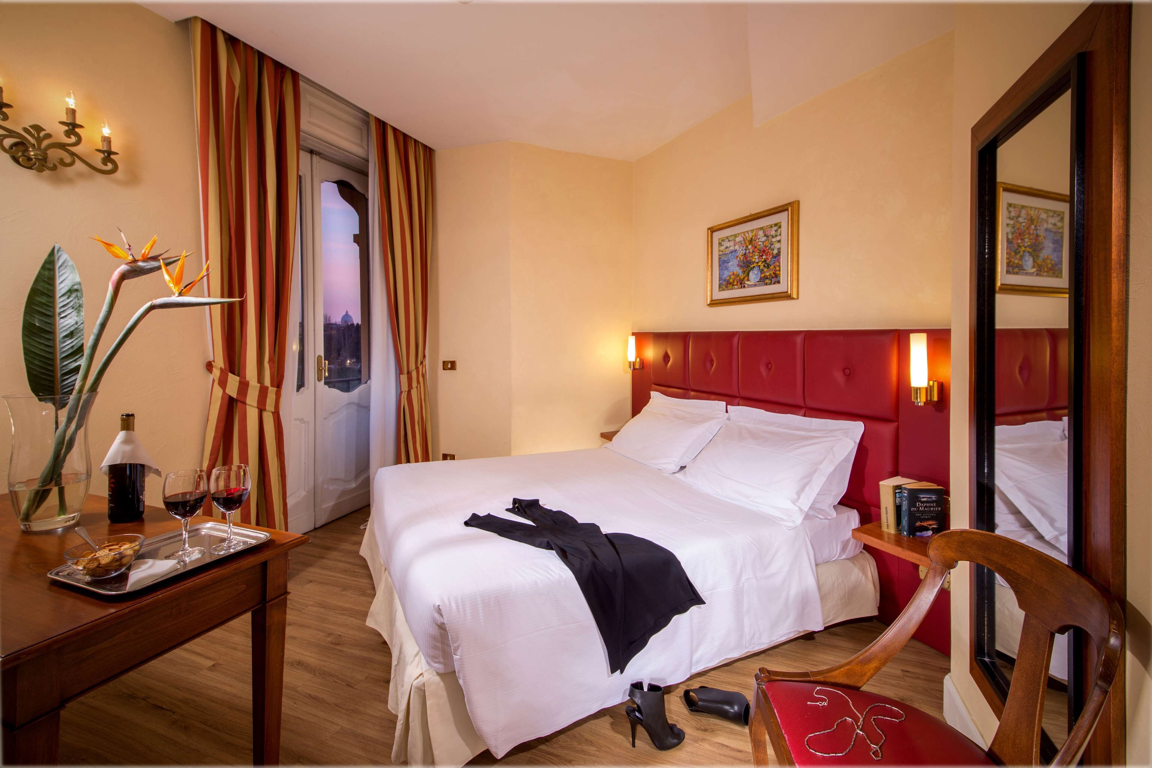 Ein Hotelzimmer mit einem großen Bett, einem Nachttisch aus Holz, einem Spiegel und einem Fenster mit Vorhängen.