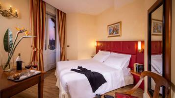 Ein Hotelzimmer mit einem großen Bett, einem Nachttisch aus Holz, einem Spiegel und einem Fenster mit Vorhängen.
